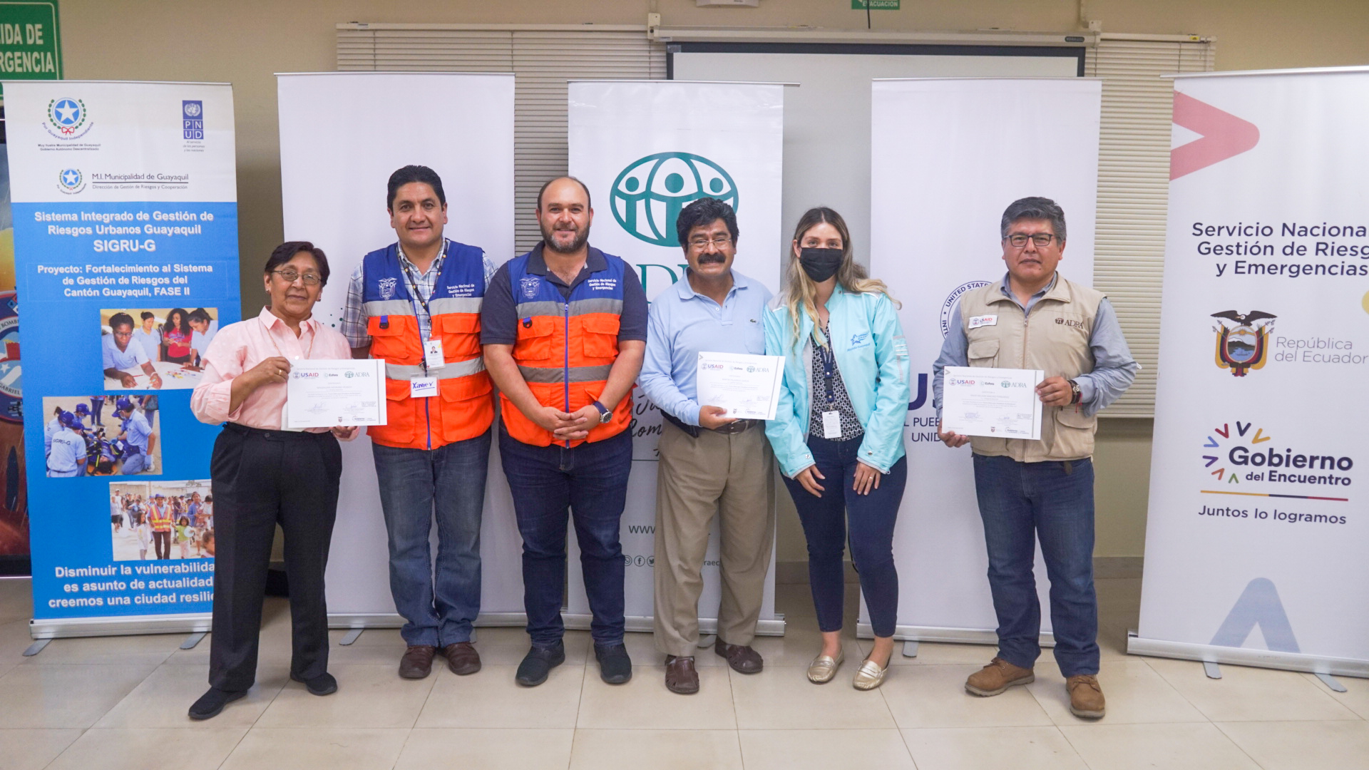 A group of six people, including Magdalena Medrano, Martin Villarroel and David Sánchez, stand in front of some rollup banners. 