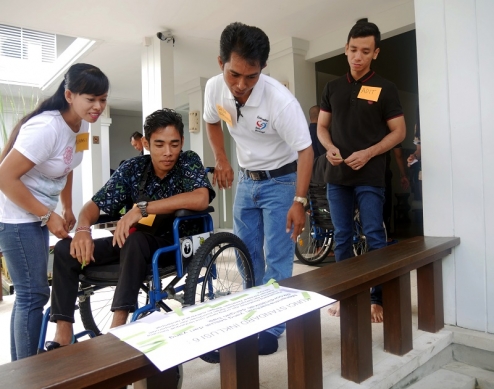 Cuatro participantes de un taller, uno de los cuales está en silla de ruedas, miran información en un cartel. 